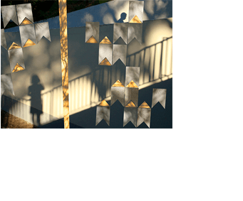 Colagem de uma composição de mastro e bandeirinhas de Volpi sobre uma foto horizontal. As bandeirinhas e o mastro foram recortados de outras fotos (de uma parede branca e outra amarela, com desenhos feitos por sol e sombras). A foto de fundo mostra duas paredes de uma rampa de garagem, com luz do sol e sombras fazendo desenhos. Alguns desses desenhos são sombras de árvores; outros são sombras das paredes, retas, que criam a ilusão de diversos planos inclinados. No alto, à direita, aparece a sombra de uma pessoa de perfil, dos ombros para cima. No canto de baixo, à esquerda, há a sombra de uma menina e de uma grade baixa, que sobe em direção à direita.
