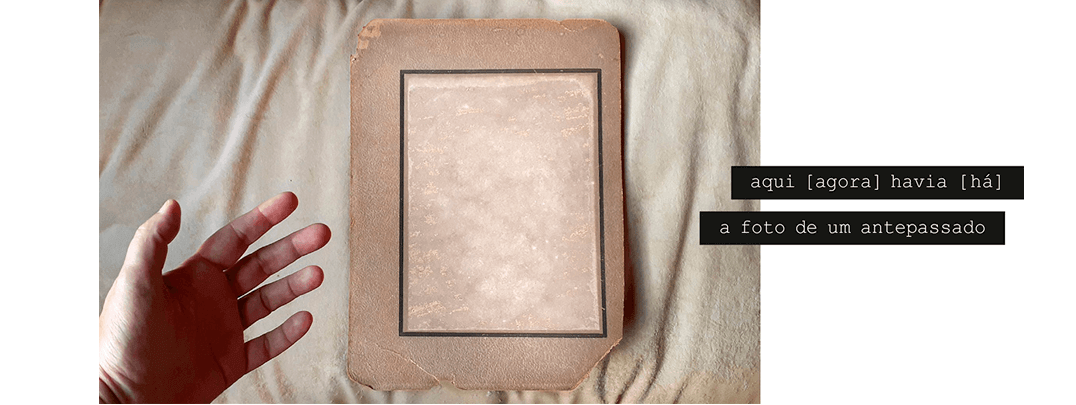 Foto horizontal e clara, em tons de bege, mostrando um grande passepartout vertical, marrom e muito velho e rasgado, com uma mancha clara e retangular no lugar onde foi arrancado um retrato. No canto esquerdo, embaixo, uma mão entra na imagem; está com a palma virada para a câmera, como quem quer pegar algo. Há uma frase escrita em duas faixas pretas que começam no lado direito e saem da margem da foto: aqui [ agora ] havia [há] a foto de um antepassado.