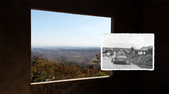 Foto horizontal do requadro de uma janela, visto de dentro de uma construção. A parede é de cimento e está bem escura, quase preta. A janela está em perspectiva, da esquerda para a direita. Lá fora vê-se uma bonita paisagem, com o cerrado em tons de marrom e verde, e morros que vão ficando azuis até sumirem no horizonte azul claro. A janela ocupa dois terços da foto. No terço restante, à direita, está colada uma foto menor, antiga, em preto e branco, mostrando uma estrada de terra em perspectiva, um carro (corcel anos 70) e uma criança sentada no capô traseiro. Vê-se uma casinha ao lado e uma pequena cidade ao longe. A foto menor está ligeiramente sobre a maior, e as linhas do horizonte das duas coincidem.