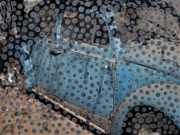 Foto horizontal de um fusca azul escuro velho, manchado e empoeirado, com luz do sol e sombras. Ele aparece de "meio perfil", com o pneu traseiro vazio. Ocupa quase todo o quadro, menos três dos cantos onde se vê o chão de asfalto. Sobre toda a superfície foram coladas bolinhas recortadas de outras fotos, em tons de azul e cinza. Estão bem próximas, seu formato é irregular e contornado por uma linha clara.