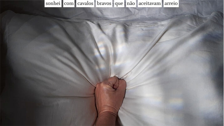 Foto horizontal colorida mostrando um punho fechado pressionando um travesseiro branco. A luz da janela faz muitas sombras escuras em toda a foto. O punho está no centro da parte de baixo. Colada à margem de baixo, centralizada, está uma frase sobre uma faixa branca: sonhei com cavalos bravos que não aceitavam arreio. (Esta é a última imagem da série.)