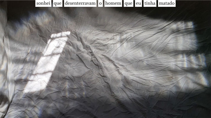 Foto horizontal colorida de um lençol branco amarrotado e parte de uma fronha no lado esquerdo. As bordas são muito escuras, chegando a ser pretas na parte de cima e no lado direito. O restante da imagem é cinza claro e cinza escuro, predominando o escuro. Há um retângulo enviezado de luz do sol na parte da esquerda. A imagem é meio sinistra. Colada à margem de cima, centralizada, está uma frase sobre uma faixa branca: sonhei que desenterravam o homem que eu tinha matado. 